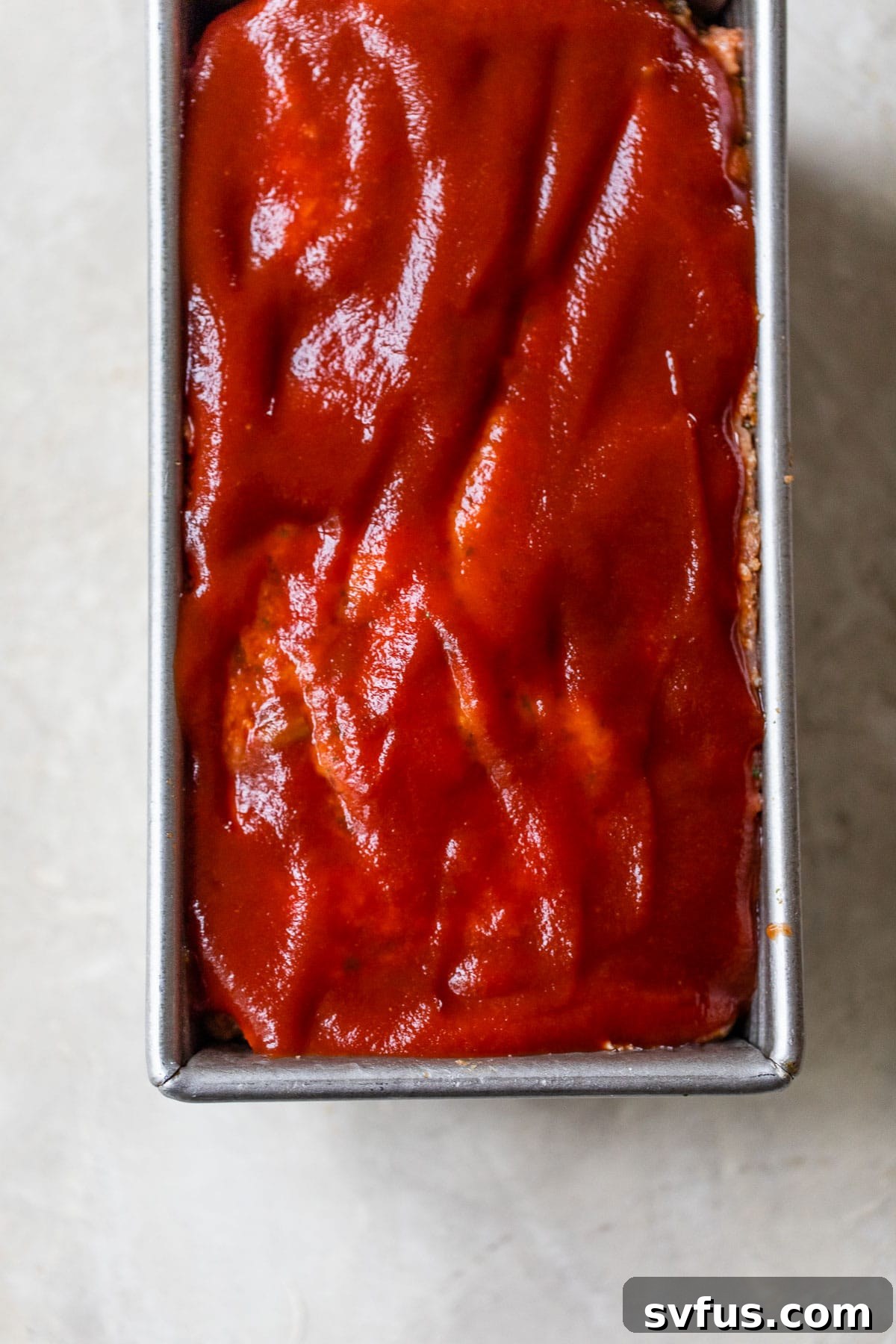 Raw meatloaf in a loaf pan with a simple ketchup glaze brushed on top, ready for baking.