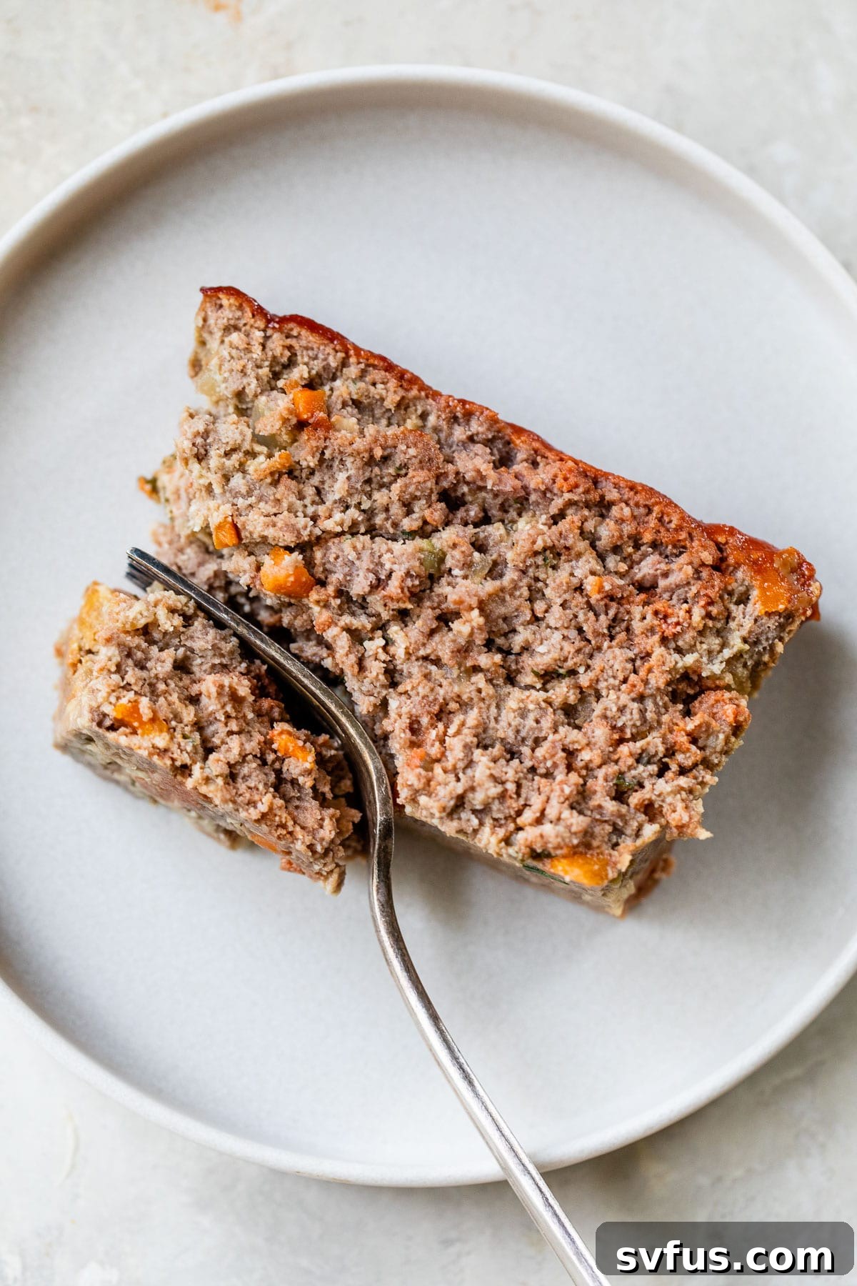 A perfectly cooked slice of Whole30 meatloaf on a white plate with a fork, ready to be eaten.