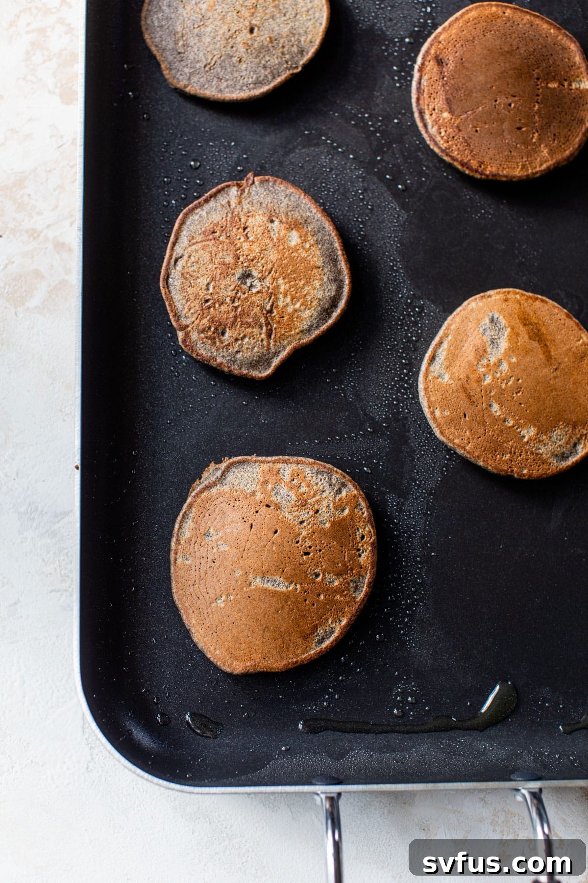 Buckwheat pancakes cooking on a hot griddle, showing bubbles forming