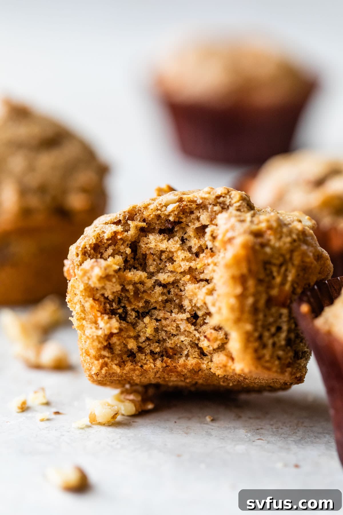 A perfectly baked carrot cake muffin with a bite taken out, revealing its moist interior and pieces of carrot and walnut.