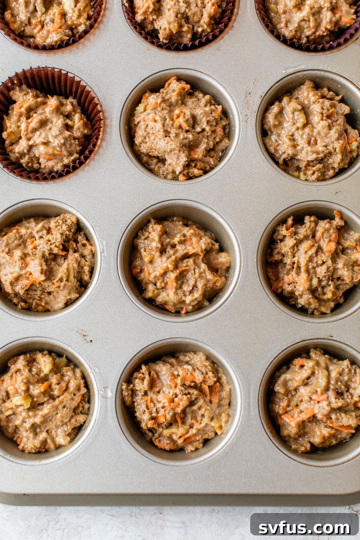 Muffin batter filled with carrots and walnuts, scooped into a lined muffin tin, ready for baking.