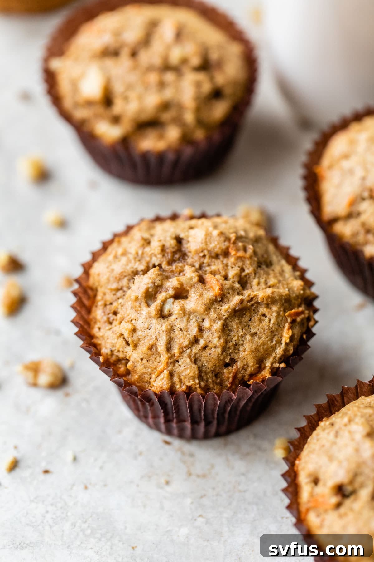 A close-up shot of a wholesome carrot cake muffin, showcasing its golden-brown top, moist texture, and visible specks of carrot and walnut.