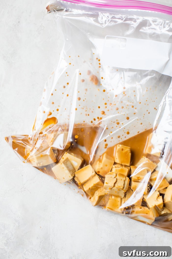 Cubed tofu being coated with tamari and cornstarch inside a clear plastic bag