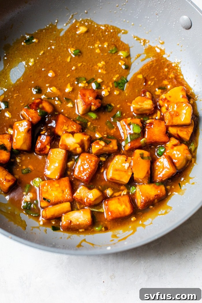 Tofu simmering in a skillet, coated in a thick, glossy Asian sauce