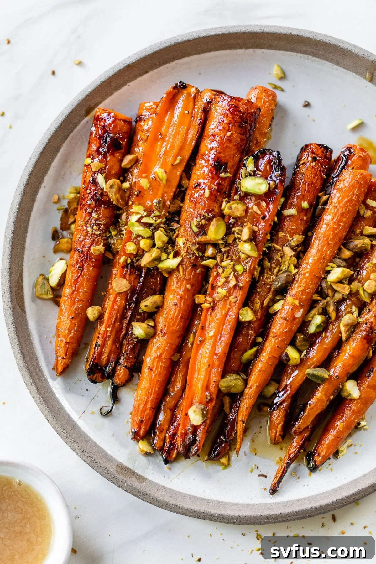 Vibrant roasted carrots adorned with a maple glaze and chopped pistachios on an elegant serving plate.