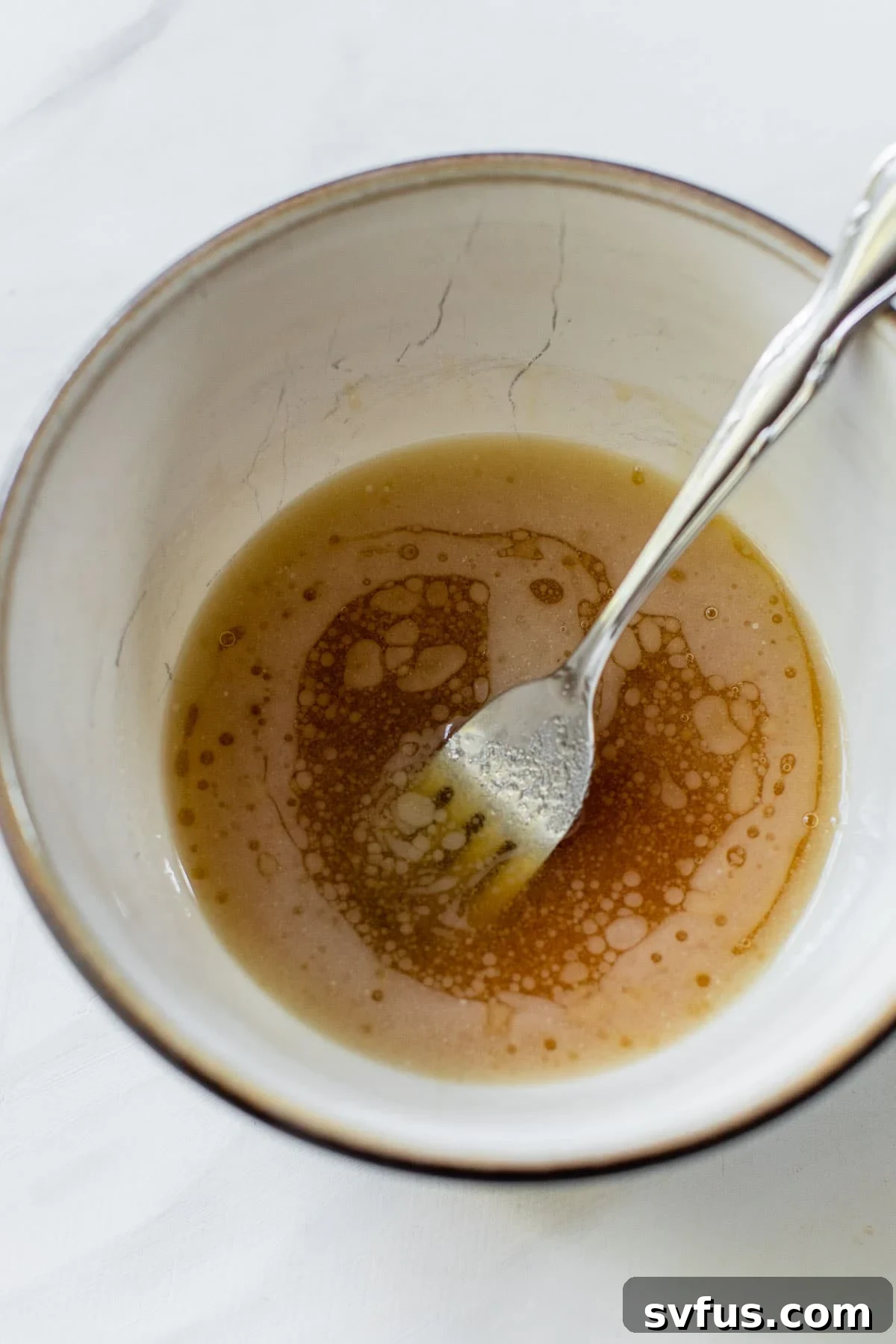 Close-up of a small bowl containing melted butter, golden maple syrup, salt, and black pepper, ready to be whisked into a savory-sweet glaze.