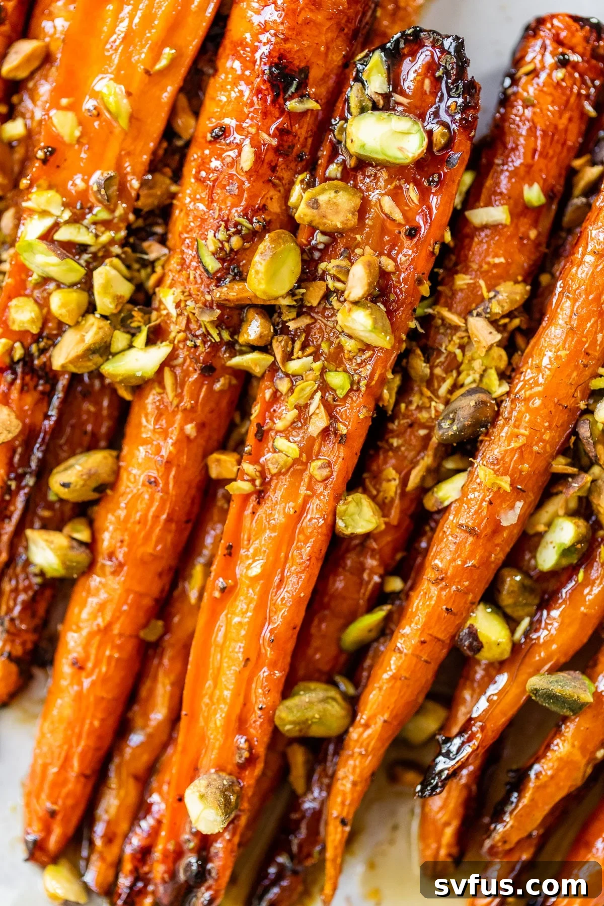 A close-up view of glistening maple roasted carrots, garnished with vibrant green pistachios, ready to be served.