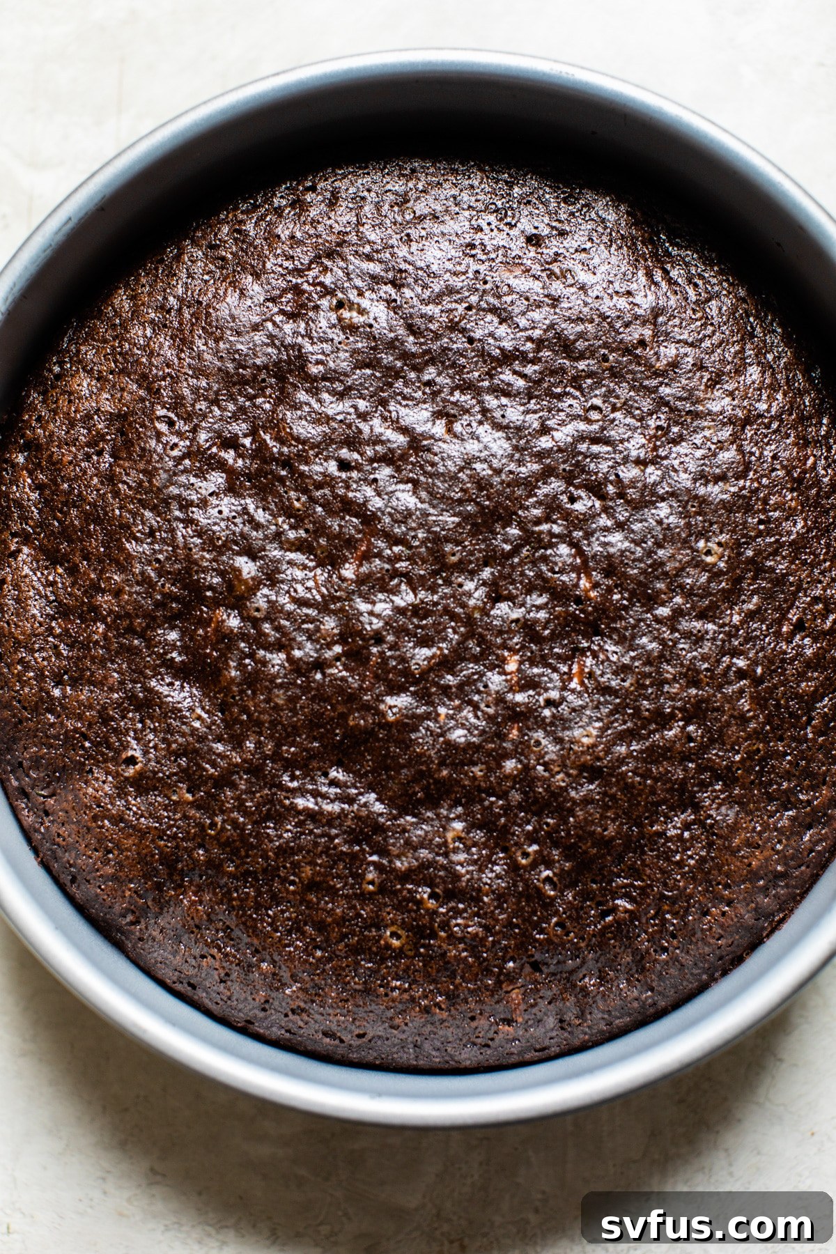 Freshly baked vegan chocolate zucchini cake layer resting in a metal cake pan on a cooling rack.