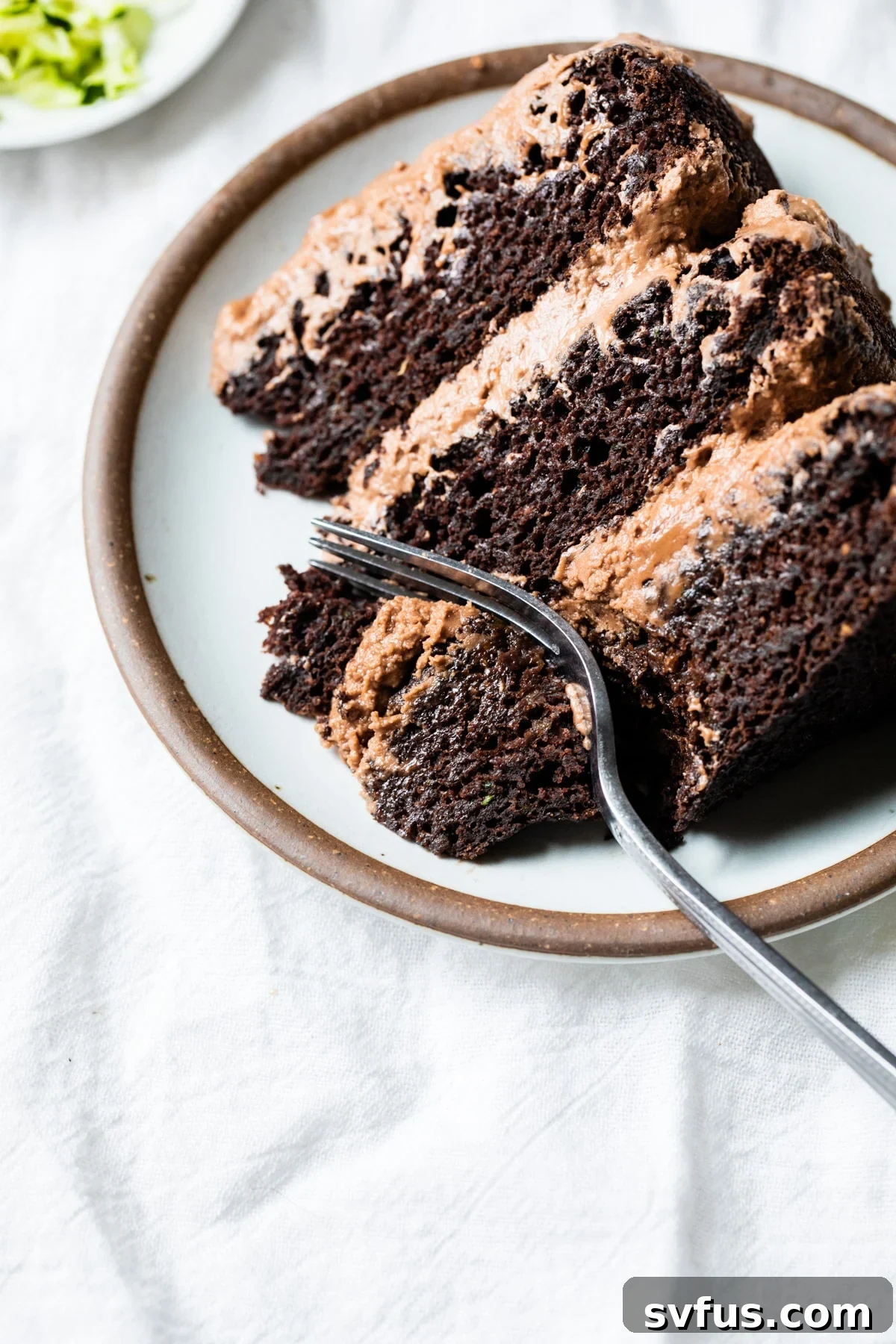 A perfectly sliced piece of Vegan Chocolate Zucchini Cake on a white plate, showcasing its moist layers and rich frosting.