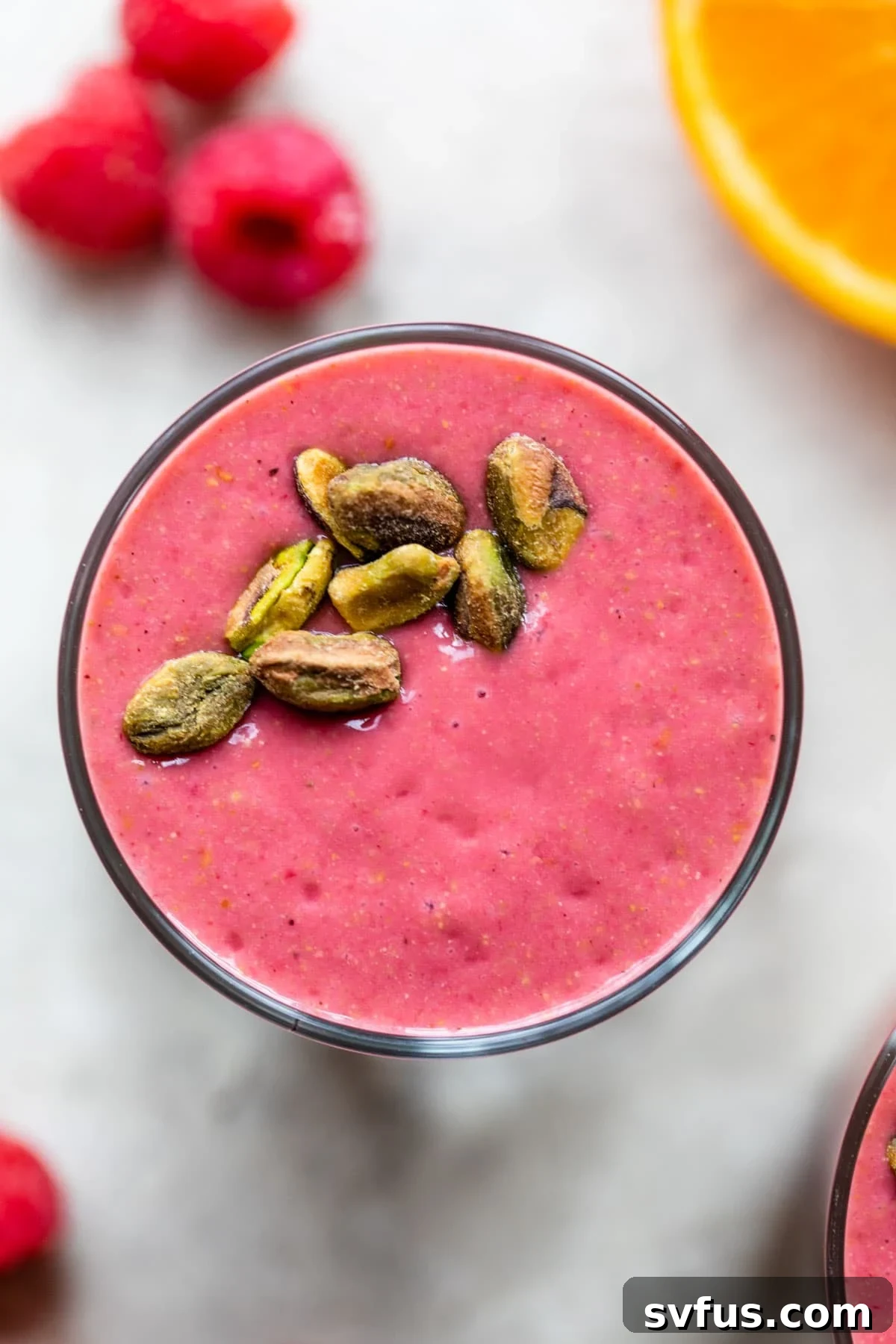 Vibrant berry pistachio smoothie in a glass, garnished with crushed pistachios and fresh raspberries.