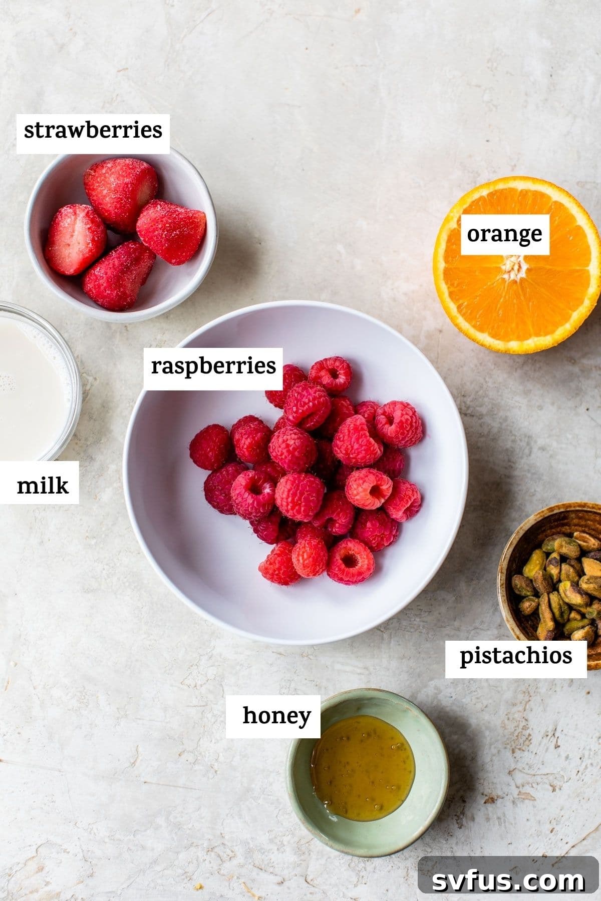 Fresh ingredients laid out for a berry pistachio smoothie, including colorful berries, a halved orange, and shelled pistachios.