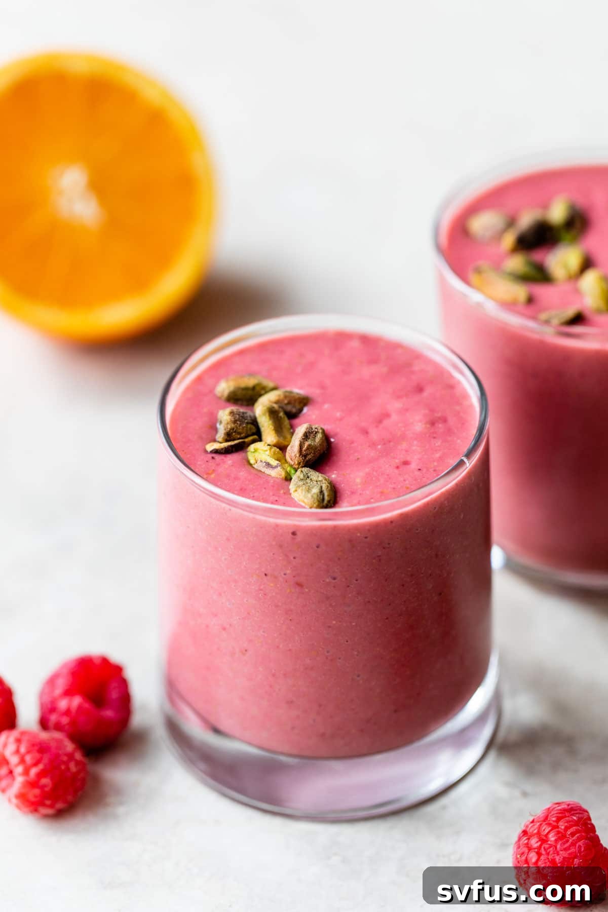 A vibrant raspberry orange smoothie in a tall glass, beautifully topped with crushed pistachios.