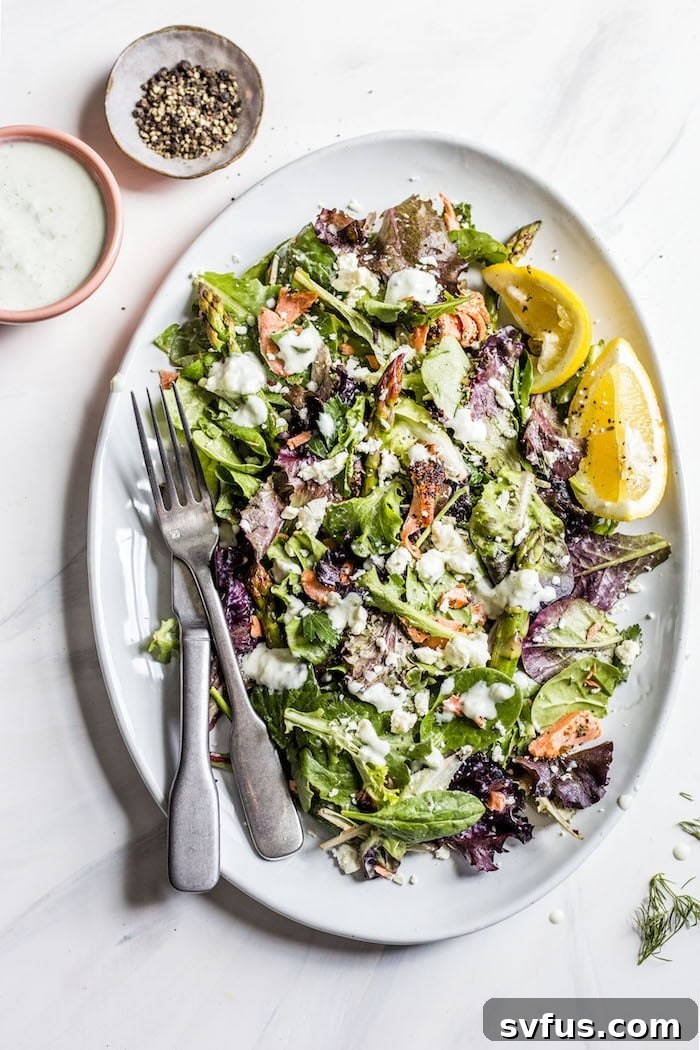 A beautifully presented plate of Garlic Salmon Salad topped with seared salmon, fresh asparagus, and drizzled with tzatziki sauce.