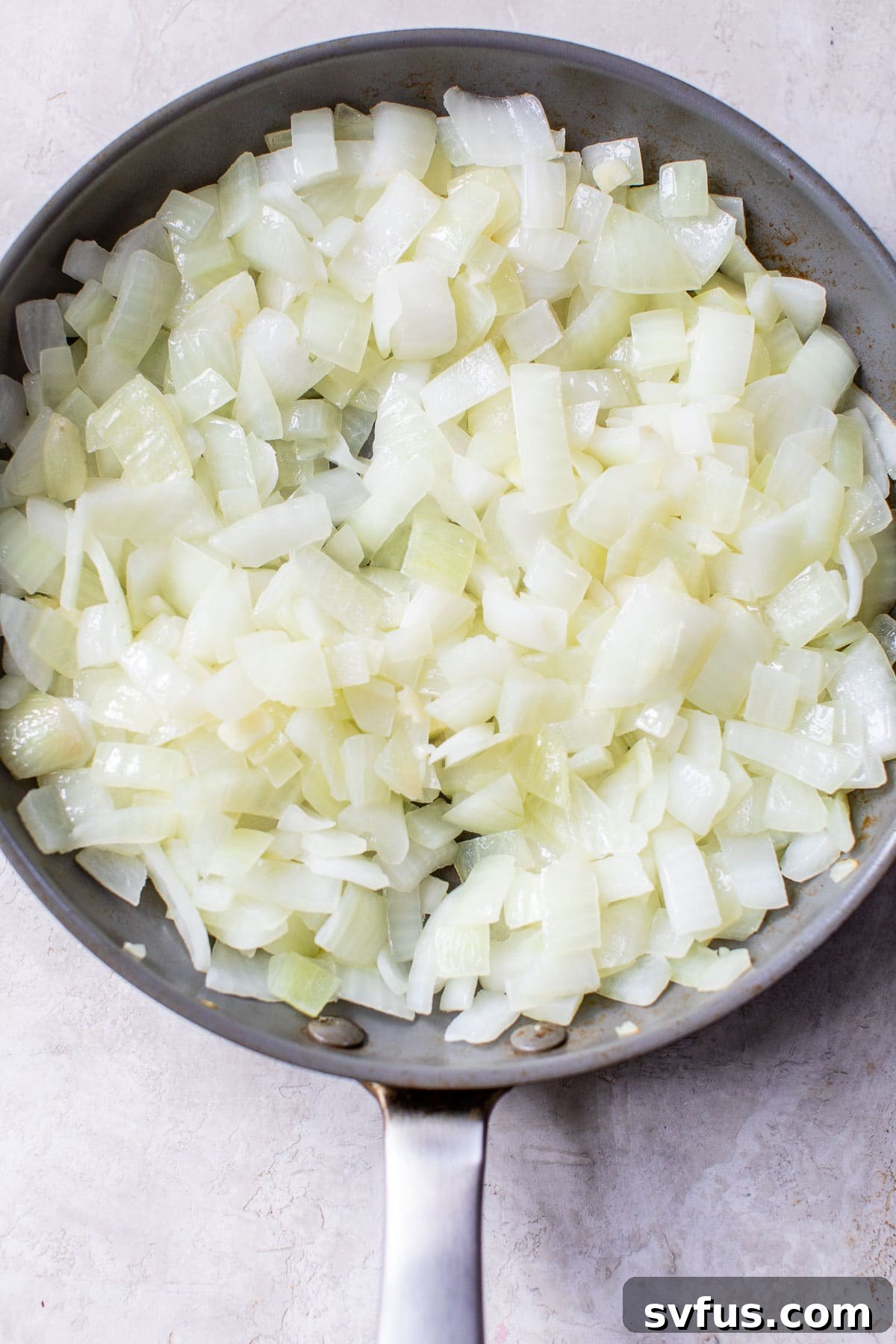 Close-up of chopped yellow onions gently sautéing in a large skillet, turning soft and translucent.