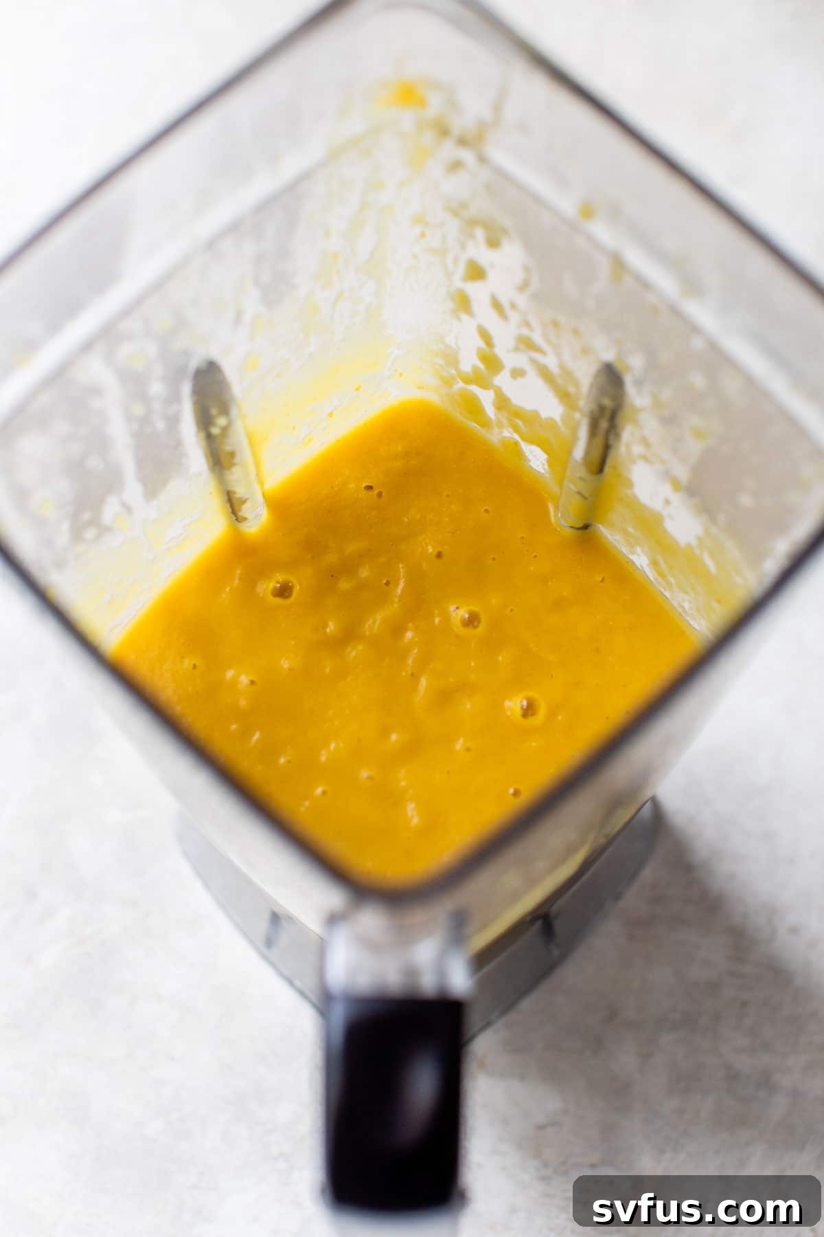 Vibrant orange blended soup swirling smoothly in a blender, showing its creamy texture.