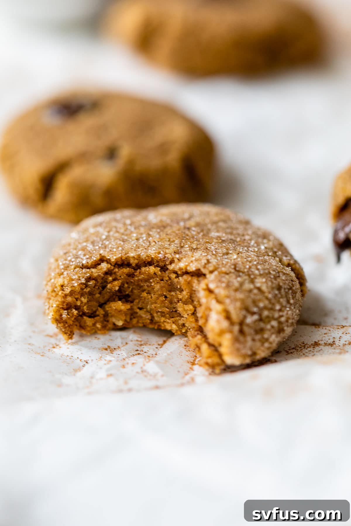 a freshly baked pumpkin cookie on parchment paper with a bite taken out of it, showcasing its soft interior