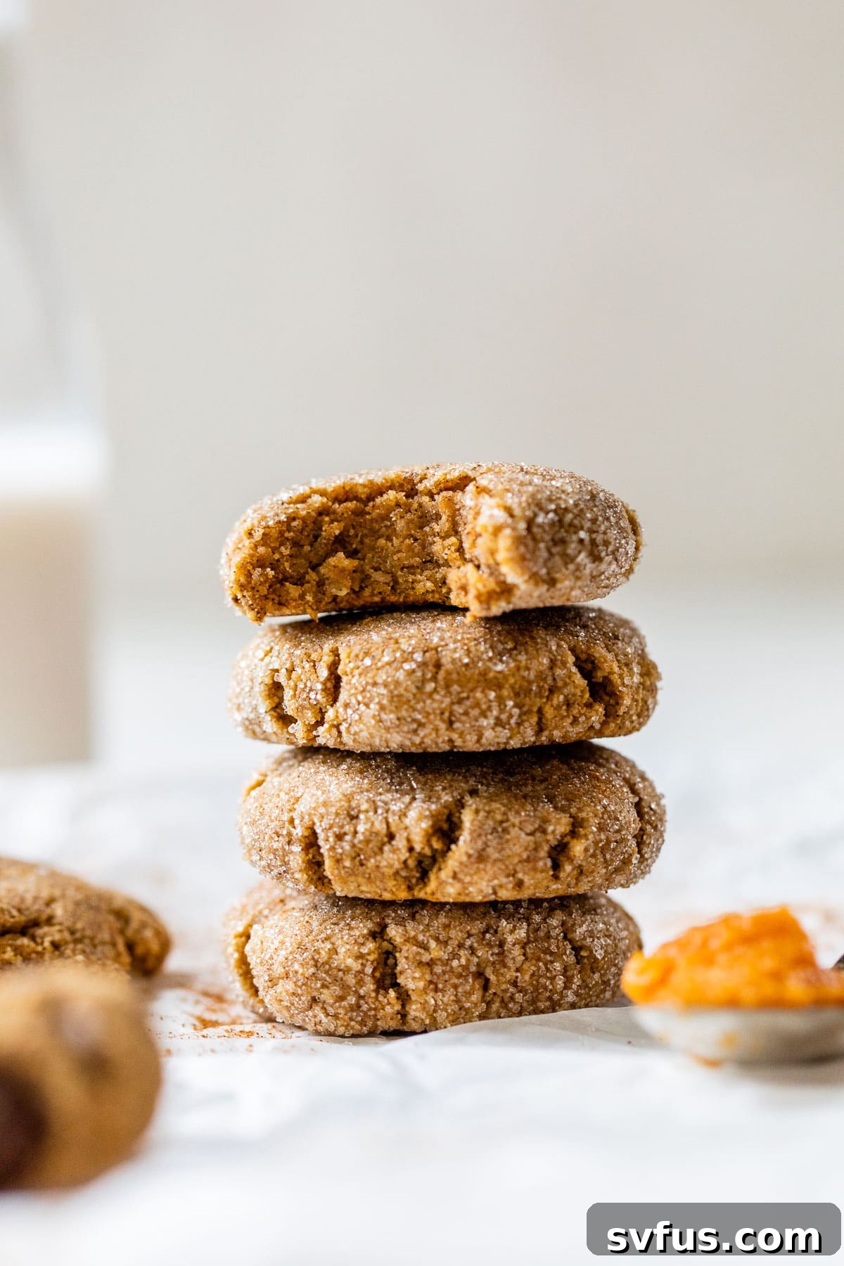 a perfectly stacked pile of healthy pumpkin cookies, with a bite taken out of the top one to show its tender interior