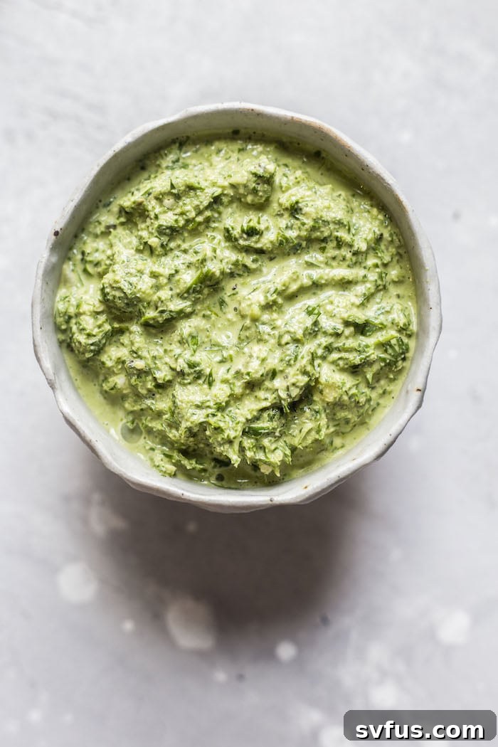 Close-up of perfectly roasted carrots, glistening with olive oil and a sprinkle of salt, arranged artfully on a light background. Some green pesto is visible in the background, hinting at the delicious topping.
