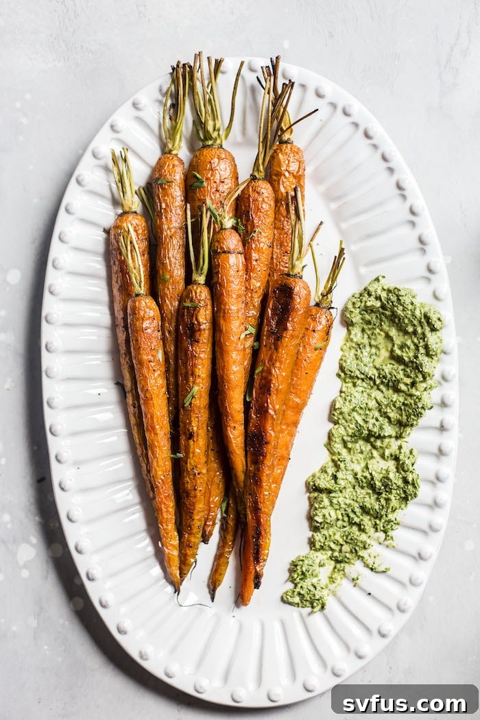 A serving of roasted carrots generously topped with bright green carrot top pesto, ready to be enjoyed. The textures of the tender carrots and fresh pesto are clearly visible.