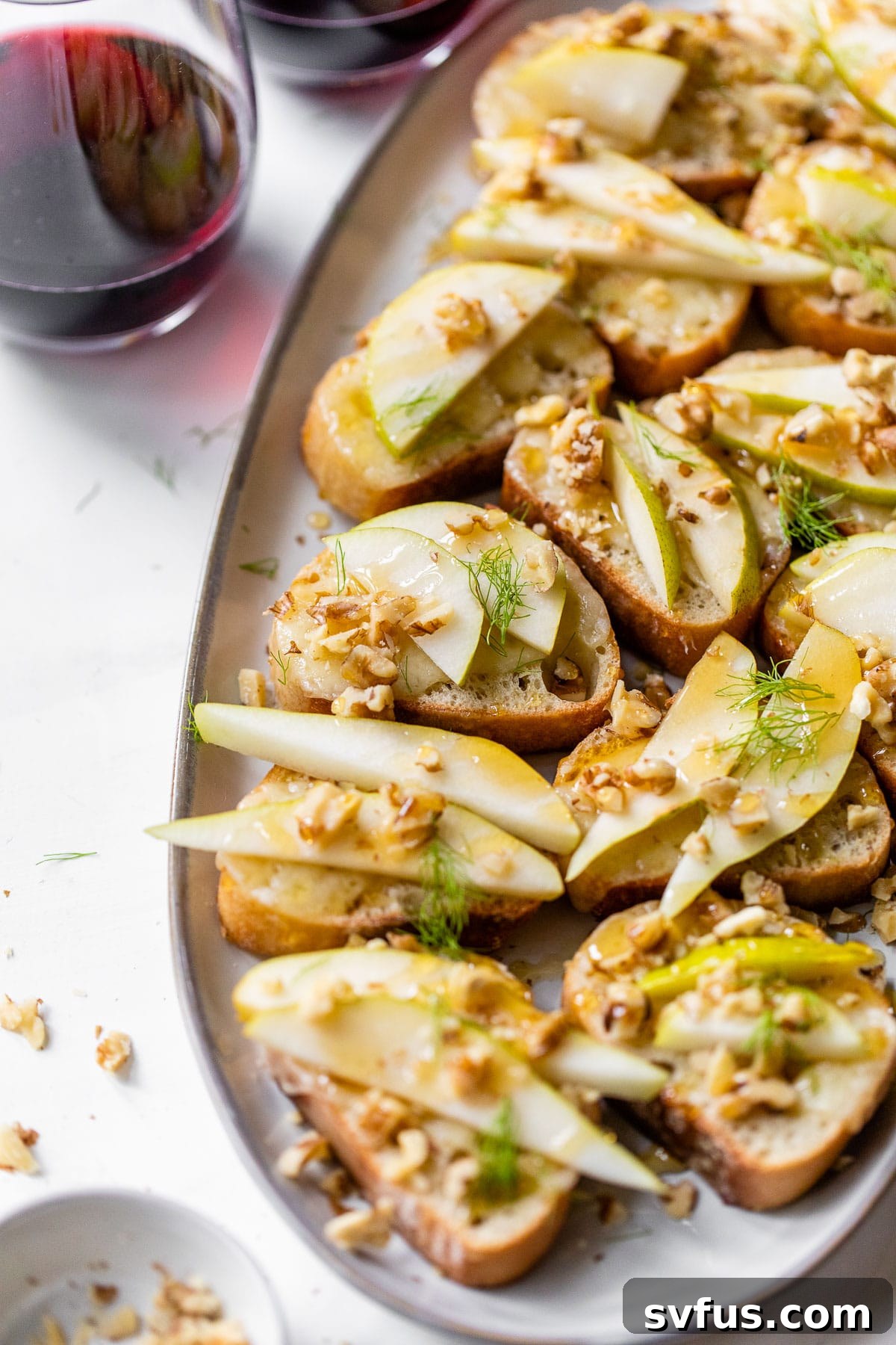Two plates of Parmesan Pear Crostini on a platter, accompanied by two glasses of red wine, setting a sophisticated ambiance.