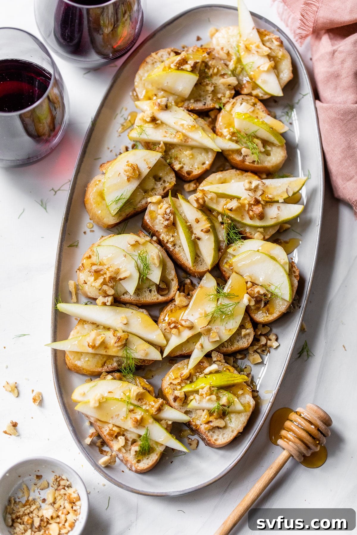 A beautifully arranged platter of Parmesan Pear Crostini, ready to serve, with two glasses of red wine suggesting a perfect pairing.