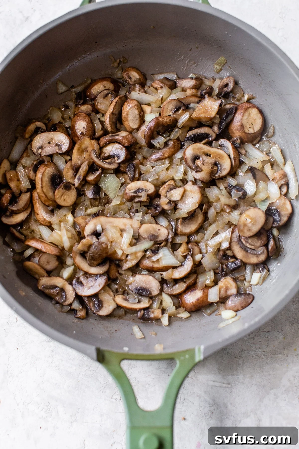 Sautéed mushrooms and onions simmering in a large skillet, forming the base of the creamy pasta sauce.