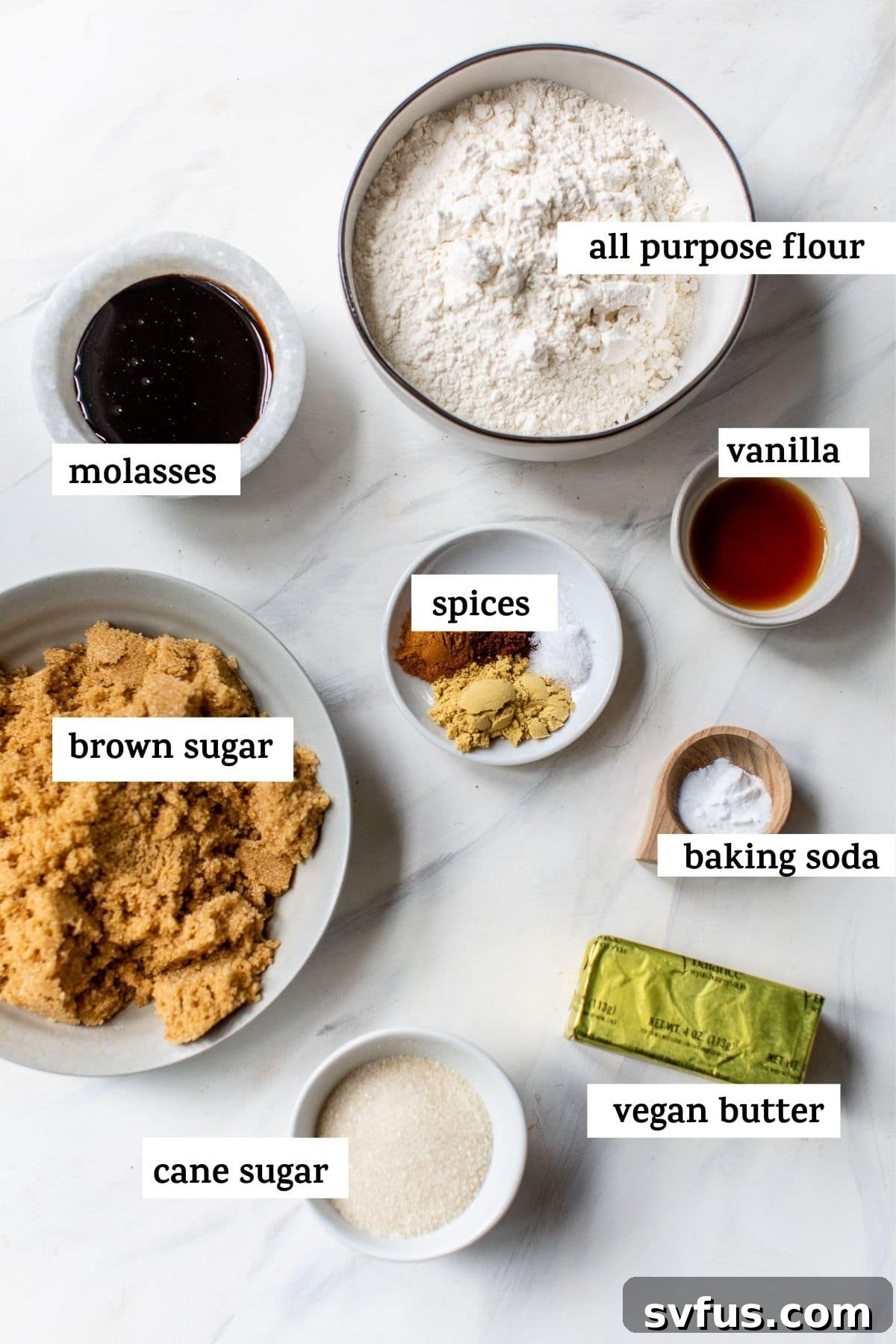 Various ingredients for making vegan ginger cookies laid out on a rustic wooden table, including vegan butter, brown sugar, molasses, flour, and spices.