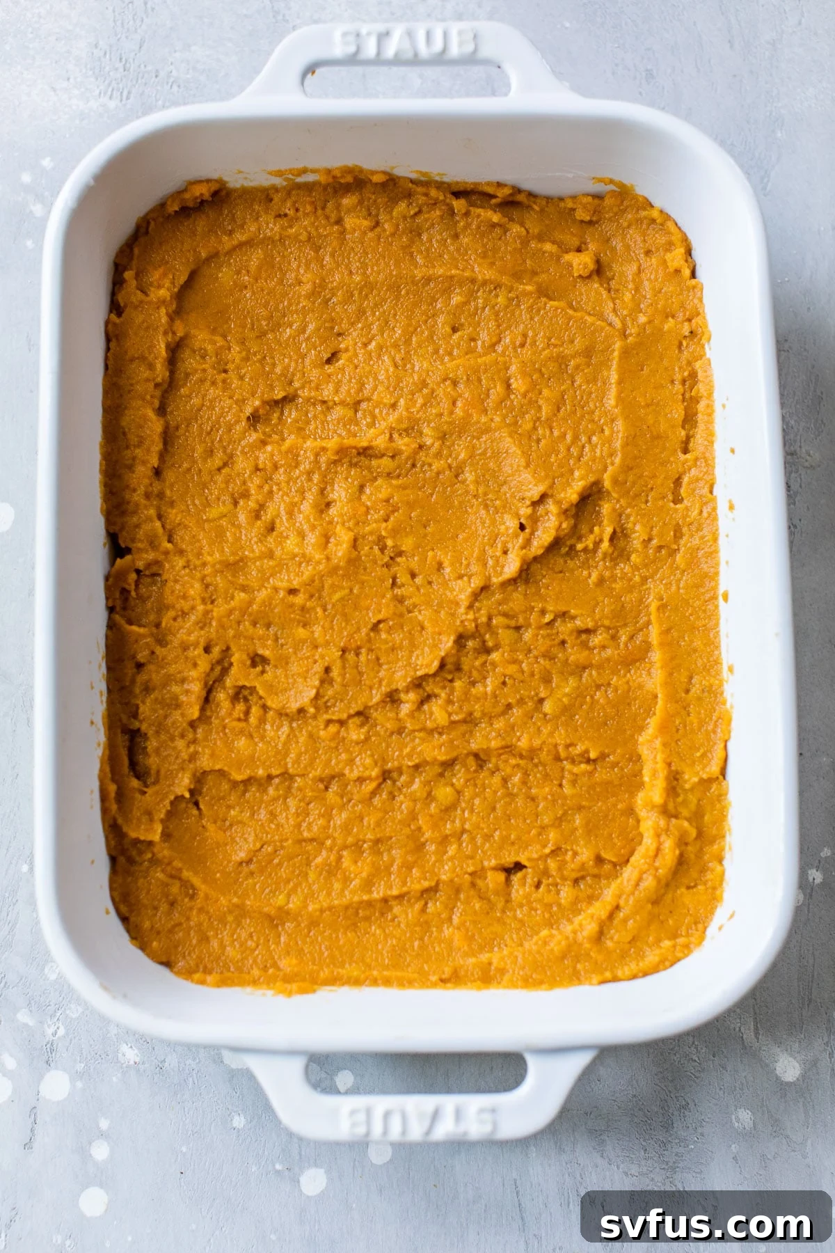 A rectangular baking dish filled with smooth, mashed sweet potatoes, ready for the topping.