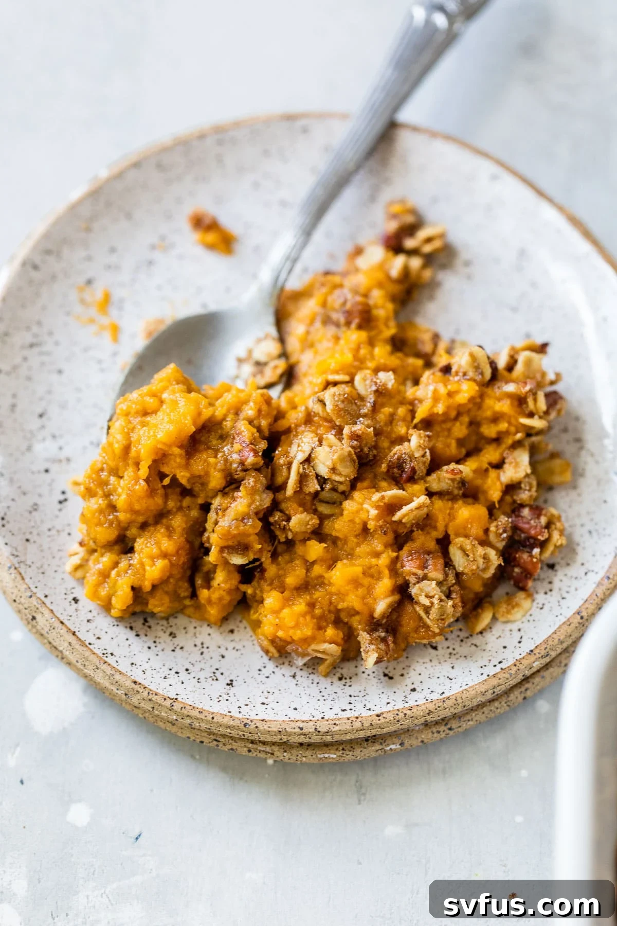 A small serving of sweet potato casserole on a white plate, showing the golden topping and smooth texture.