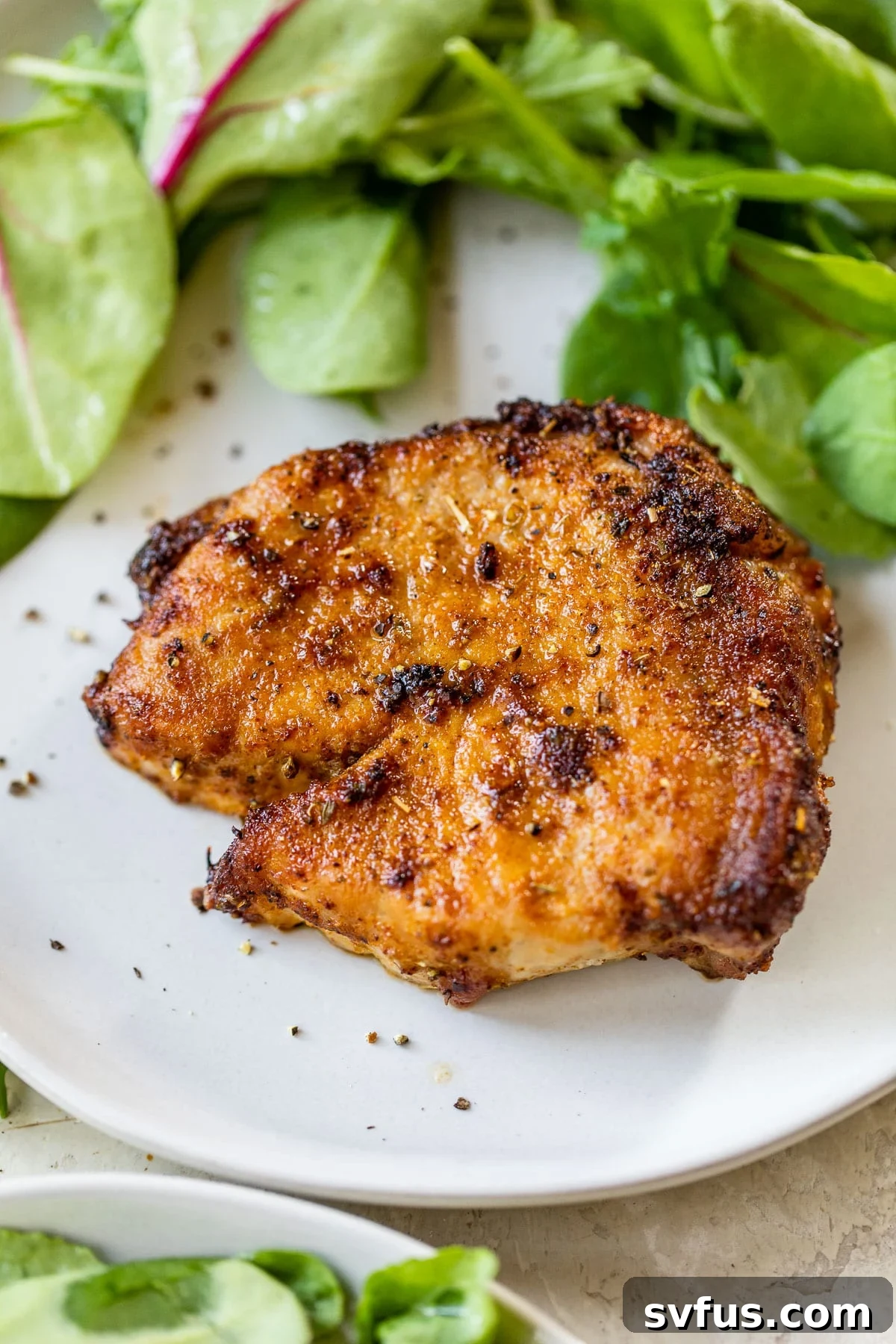 A perfectly cooked, juicy air fryer pork chop resting on a plate next to a vibrant pile of mixed greens.