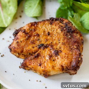 A close-up of a juicy air fryer pork chop on a plate next to fresh greens, illustrating the perfect cook.