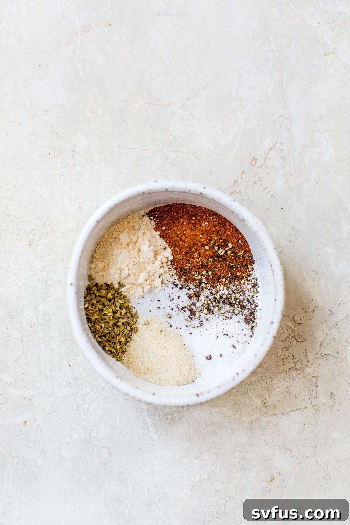 A small bowl containing a vibrant blend of paprika, garlic powder, onion powder, oregano, salt, and black pepper, ready for seasoning.