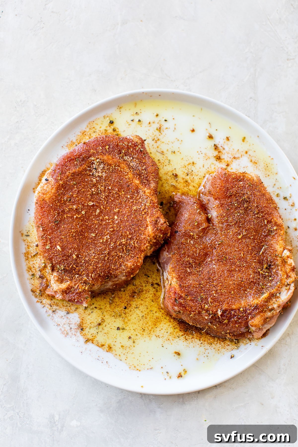 Marinated raw pork chops, generously coated with a vibrant spice rub, resting on a white plate, ready for air frying.