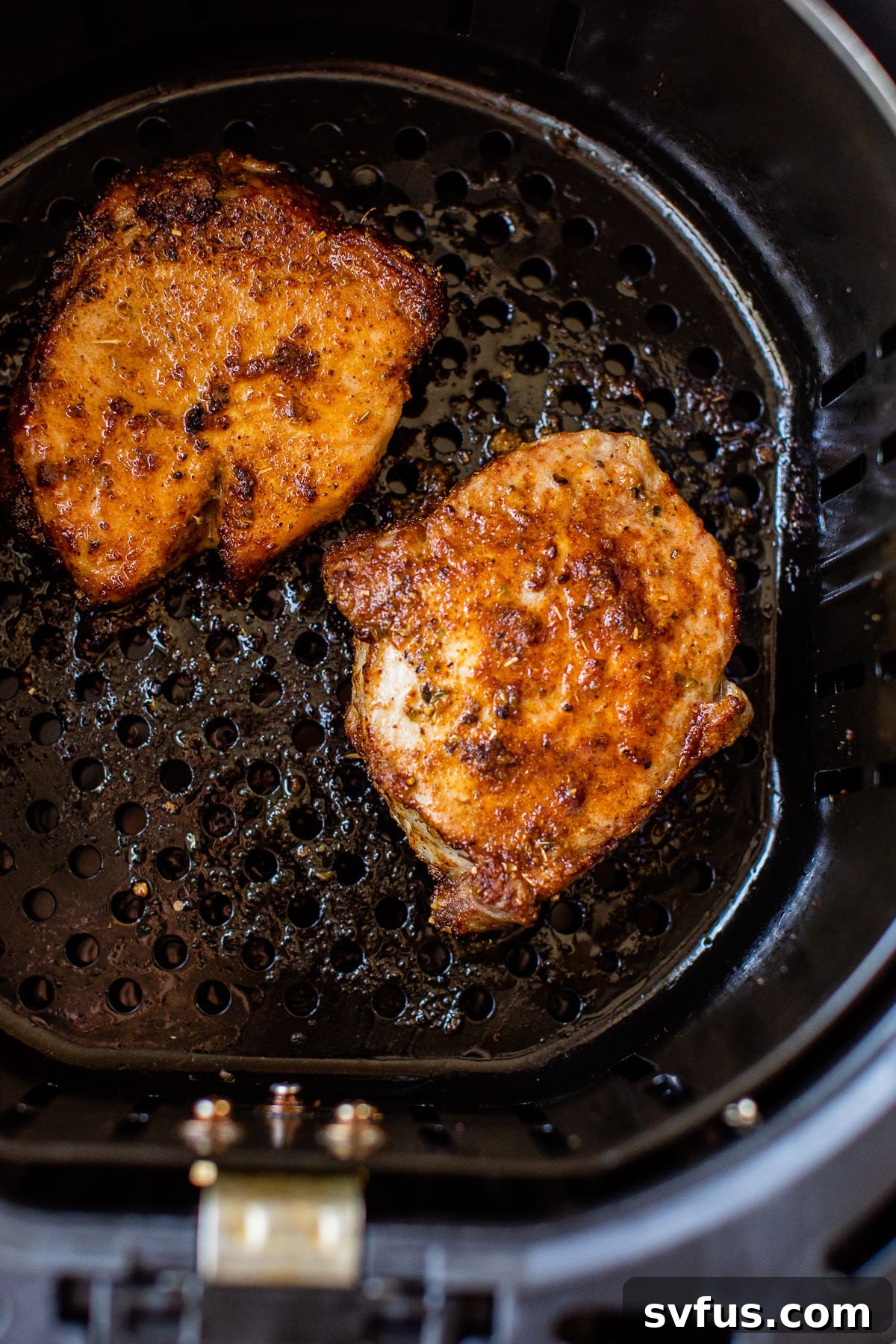 Two boneless pork chops, perfectly seasoned, cooking in a single layer inside an air fryer basket, achieving a golden-brown sear.