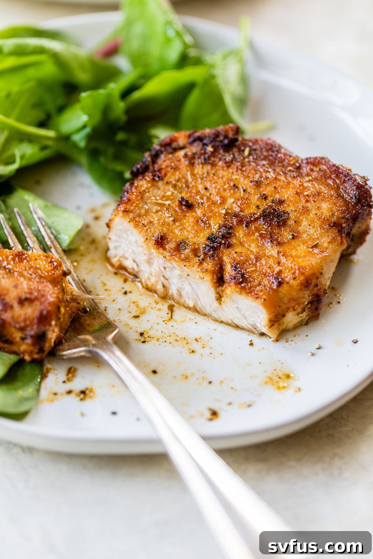 A perfectly cooked and sliced air fryer pork chop, revealing its tender, juicy interior, served on a plate alongside a fresh pile of mixed greens.