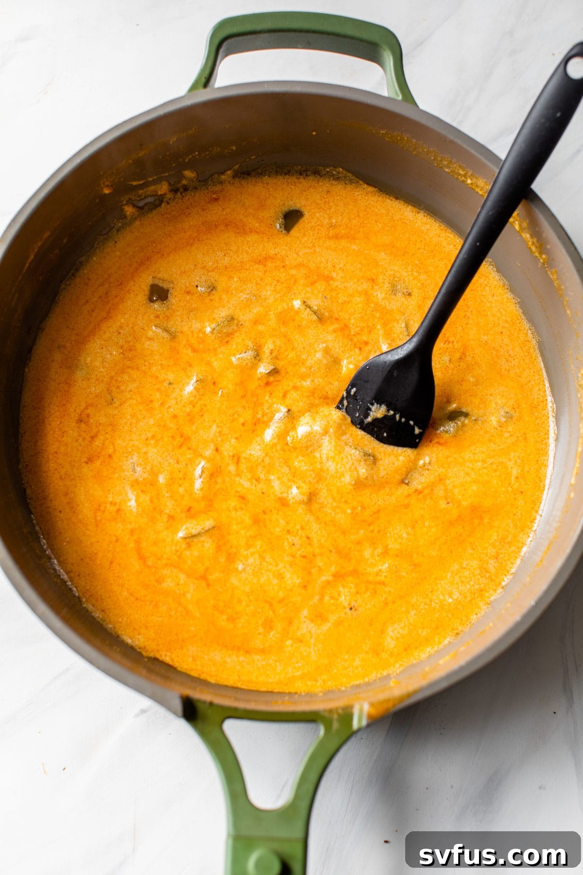 A close-up shot of the creamy, vibrant orange buffalo sauce simmering in a skillet, ready for the chicken and pasta.