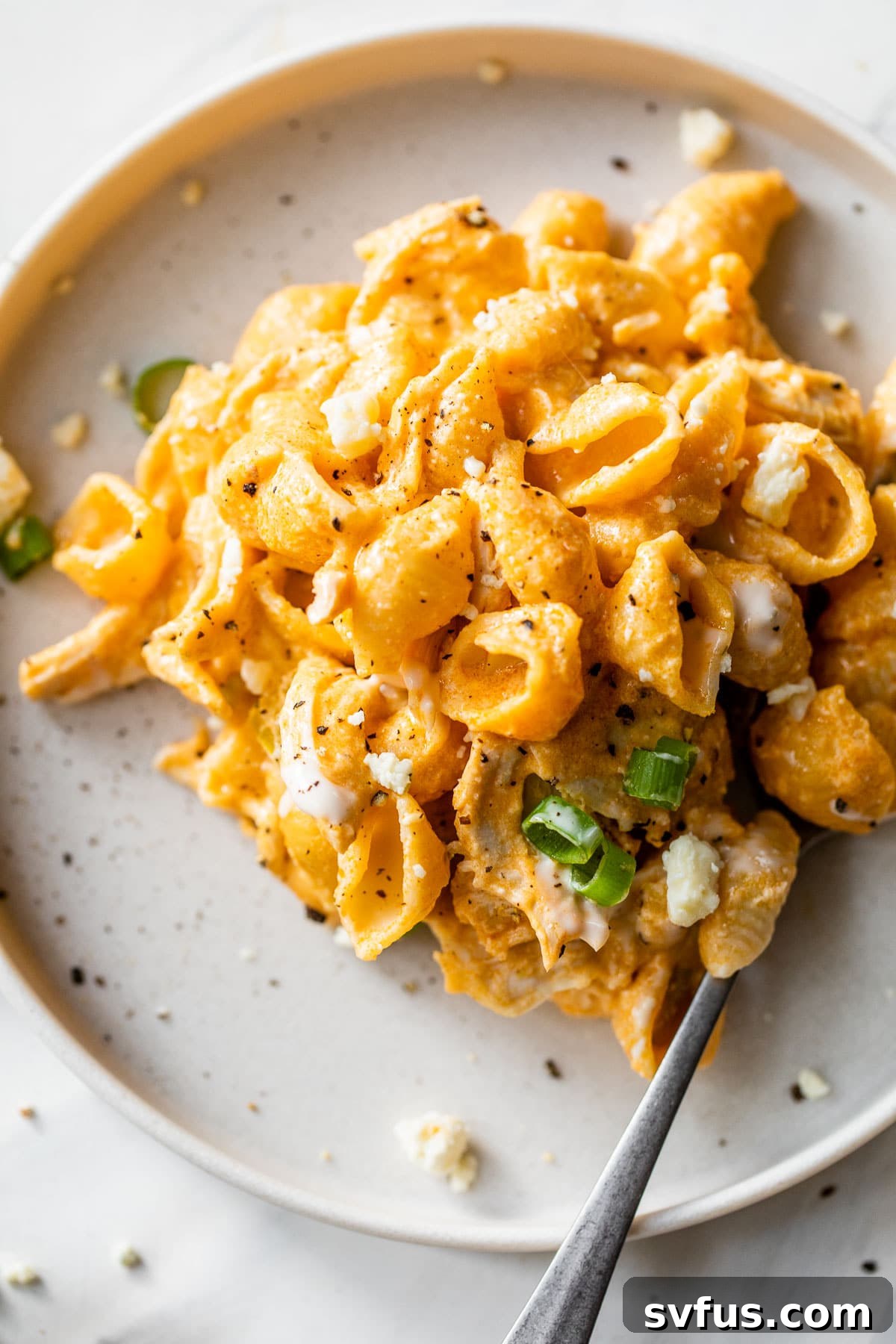 A plate of buffalo chicken pasta garnished with fresh green onions, ready for a delicious meal.