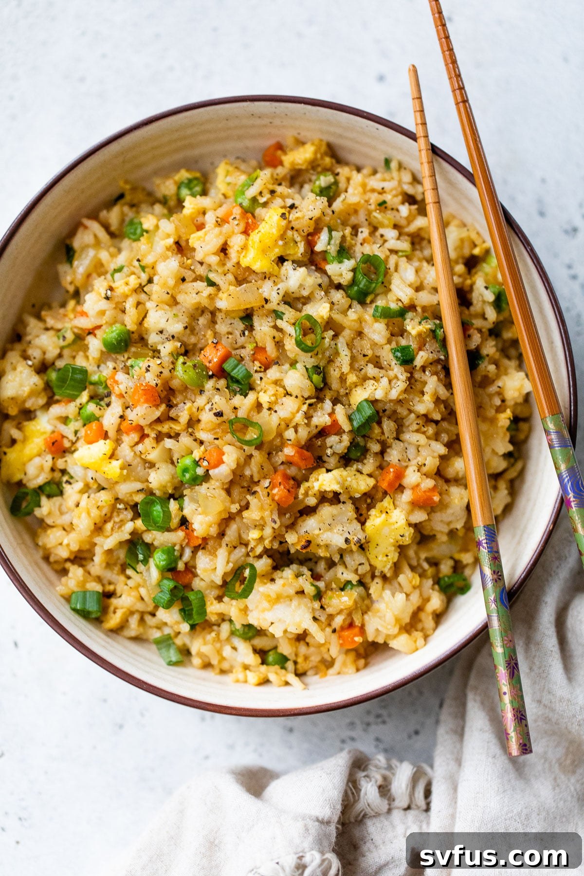 A beautifully presented bowl of Instant Pot fried rice, garnished with green onions, with chopsticks resting on top.