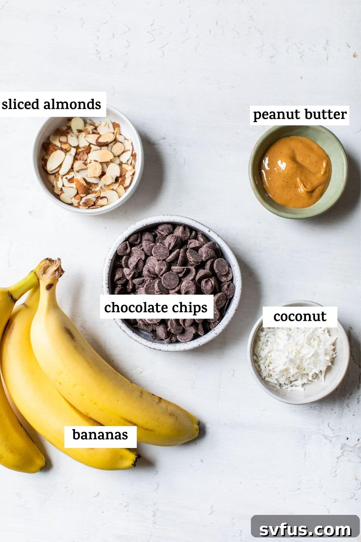A vibrant flat lay of key ingredients for chocolate peanut butter banana bites, including fresh bananas, a bowl of rich chocolate chips, creamy peanut butter, and a hint of coconut oil, all arranged on a rustic wooden surface.