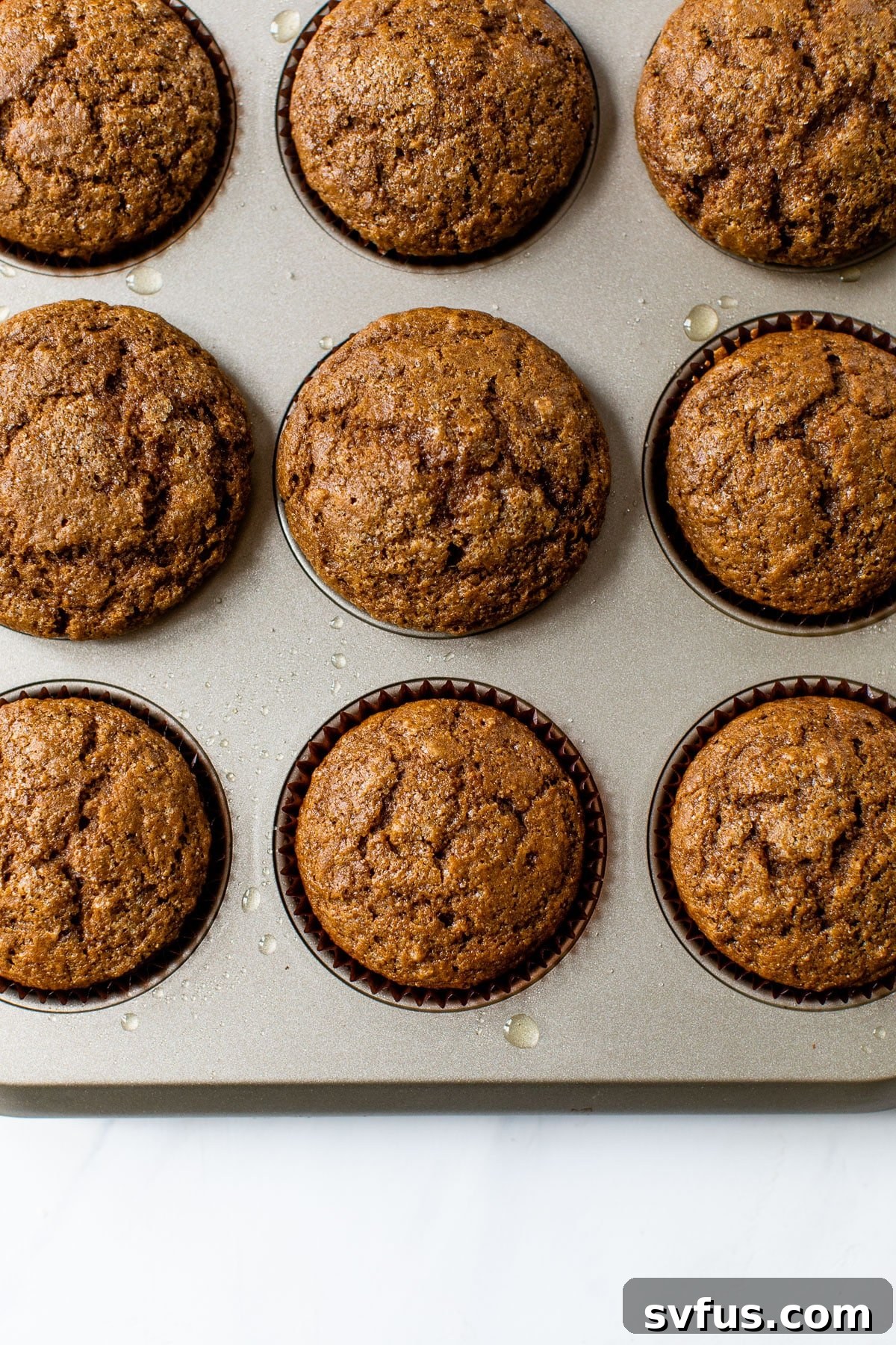 Freshly baked gingerbread muffins resting in a lined muffin tin, showcasing their fluffy texture and enticing golden-brown tops.