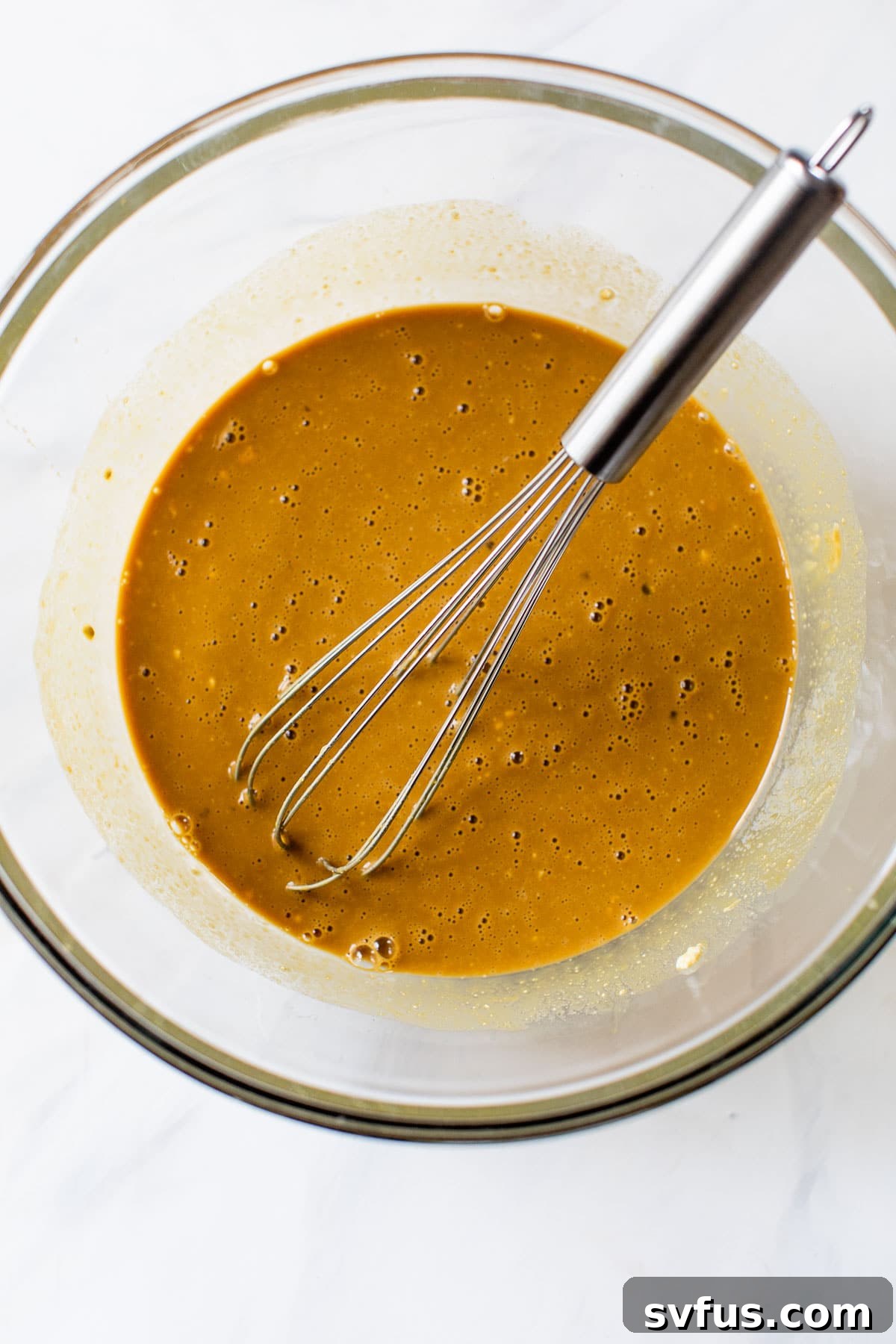 Close-up of wet ingredients like eggs, molasses, maple syrup, and vanilla extract harmoniously mixed together in a clear glass bowl, showcasing the rich color.