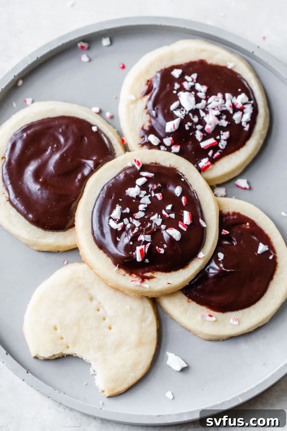 Five beautifully iced peppermint shortbread cookies on a grey plate, ready for the holidays.