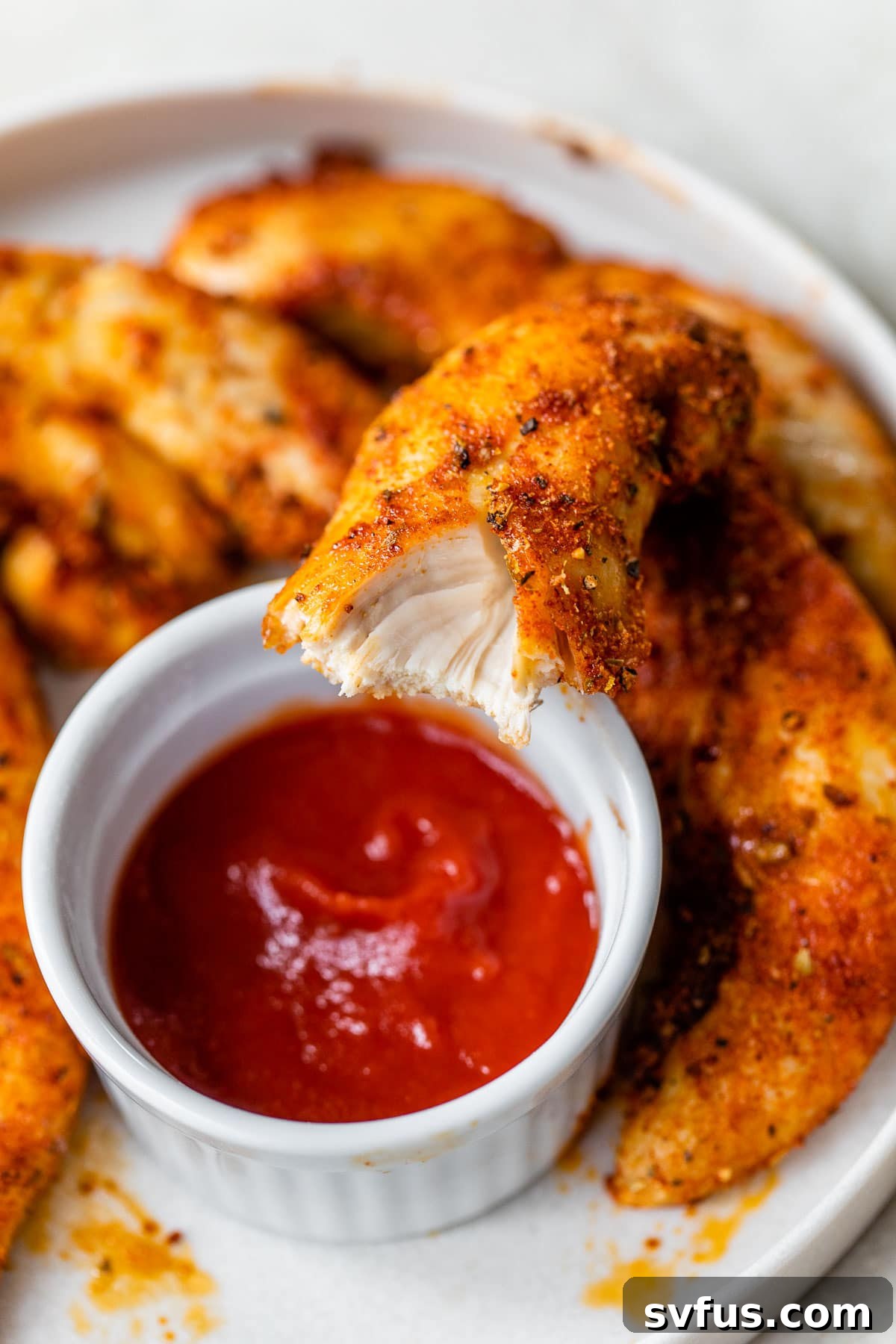 A perfectly cooked chicken tender with a bite taken out, revealing its juicy interior