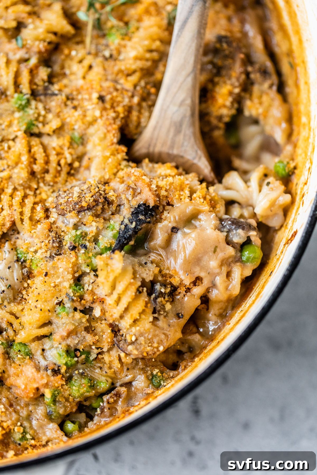 Wooden spoon scooping a portion of healthy tuna noodle casserole from a baking dish