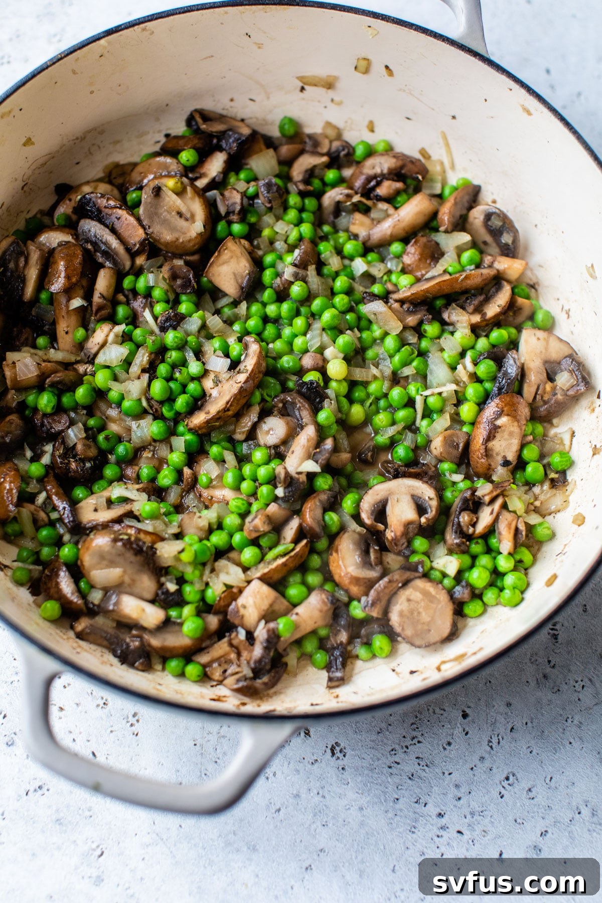 Round dish with perfectly cooked mushrooms and vibrant peas, forming the base of the casserole