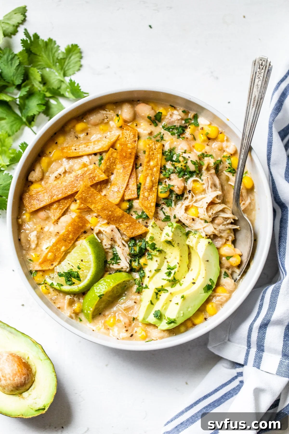 A comforting bowl of white chicken chili, elegantly topped with creamy avocado slices, fresh cilantro, and crispy tortilla strips.