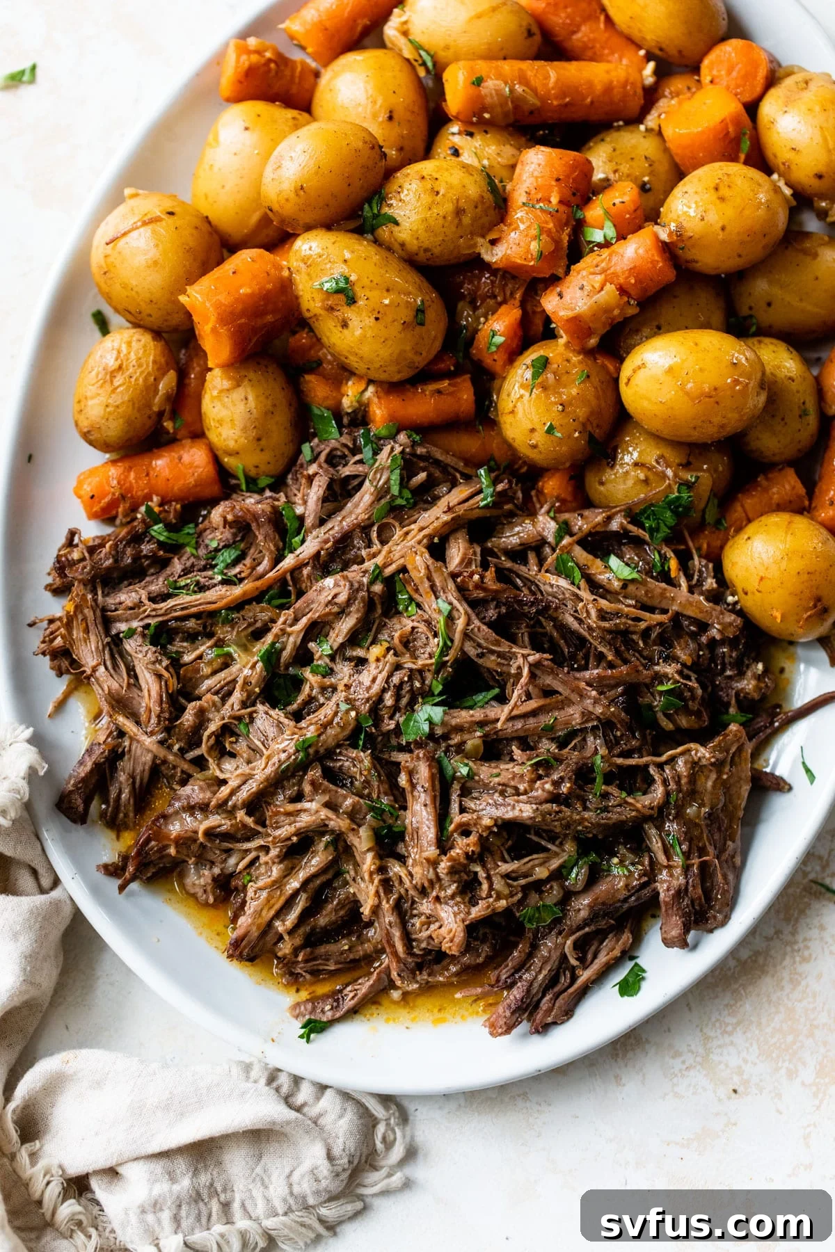 A bountiful serving platter showcasing tender shredded beef, alongside perfectly cooked potatoes and carrots, making for a classic pot roast.