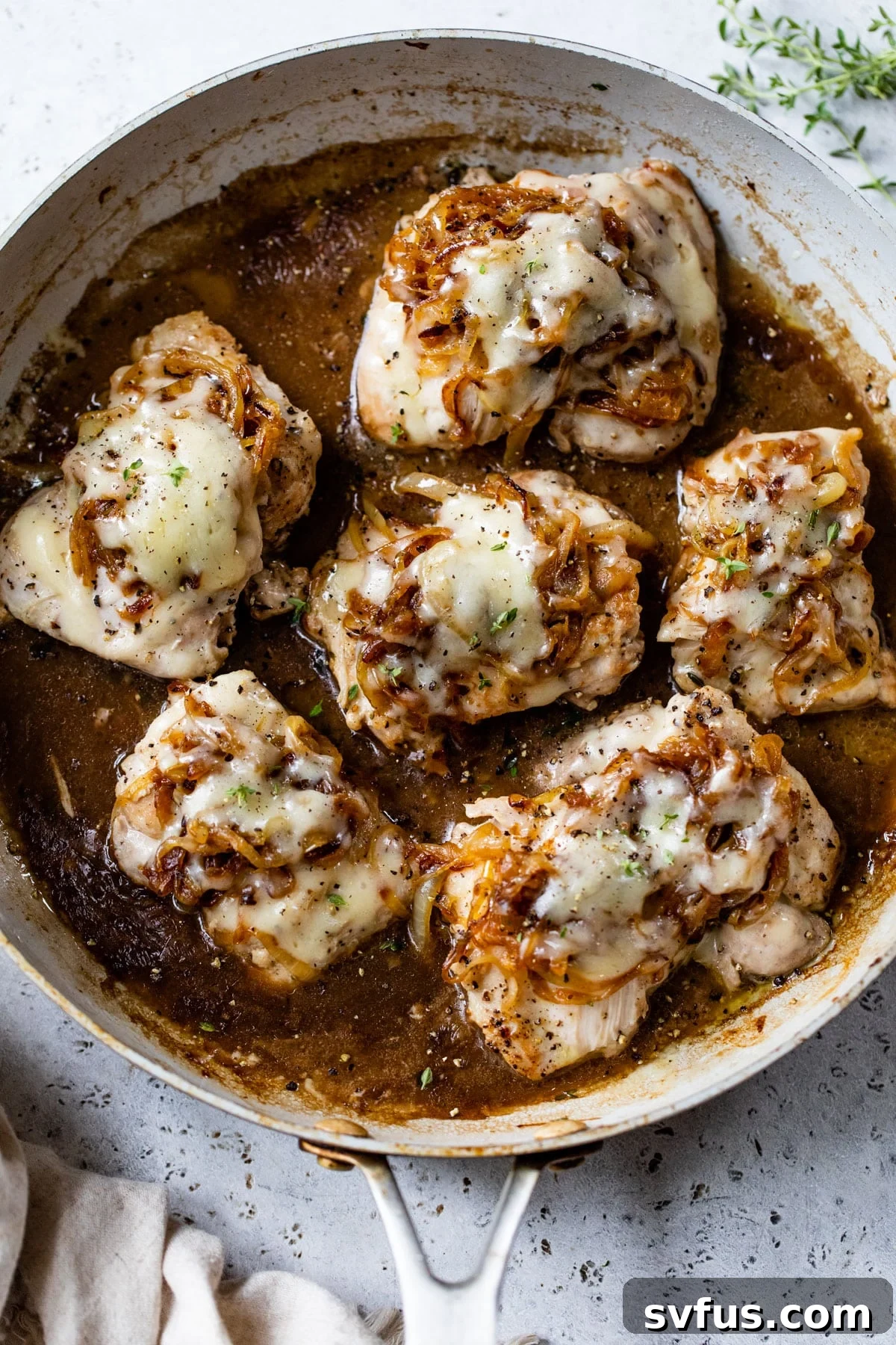 Tender, cooked boneless chicken thighs nestled in a skillet, richly topped with sweet caramelized onions and a blanket of melted cheese.