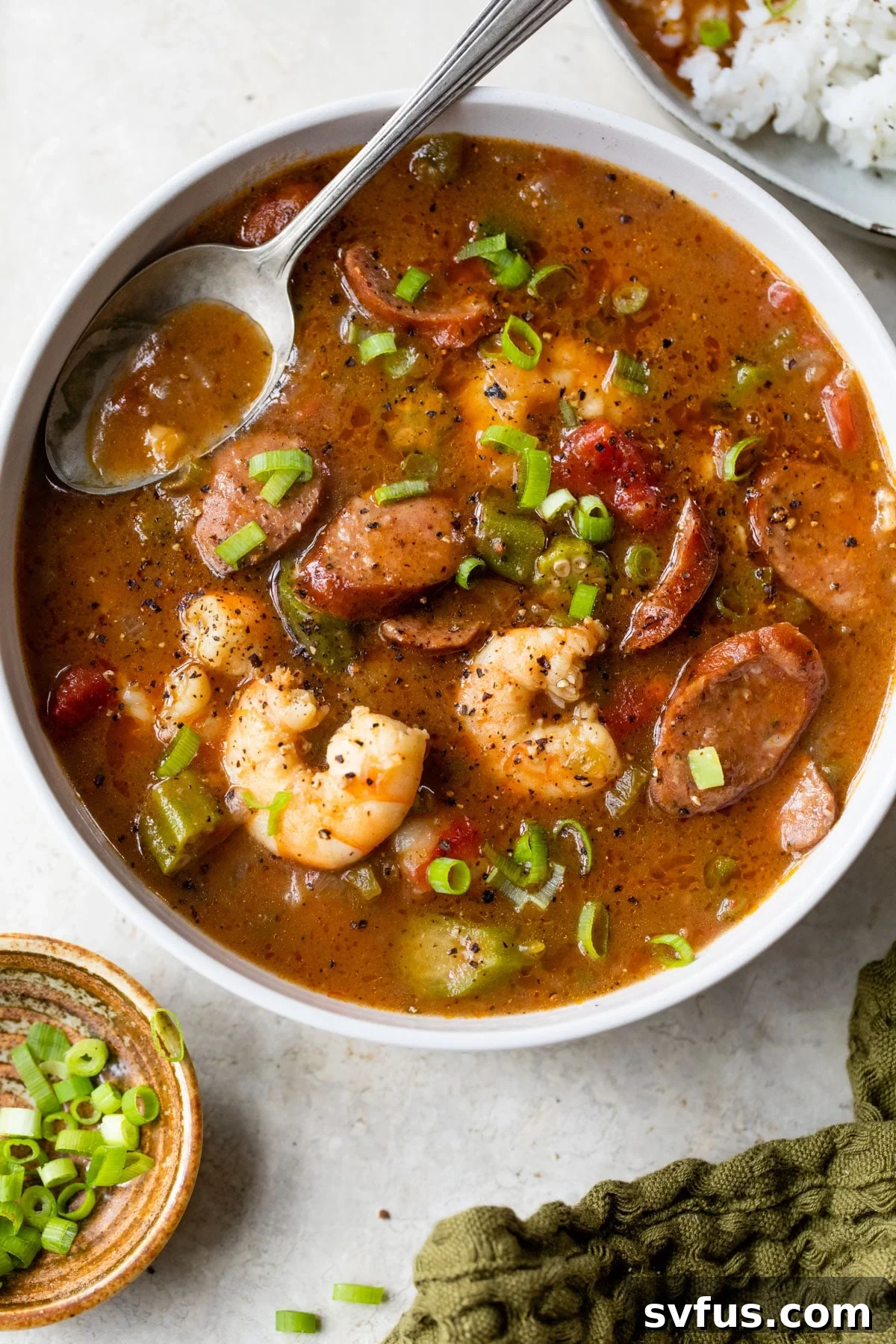 A hearty bowl of gumbo brimming with succulent shrimp and savory sausage, garnished with a side of fresh green onions.