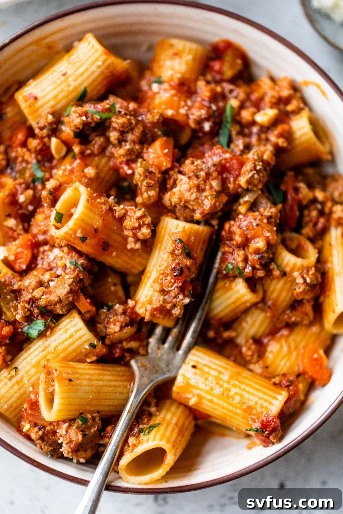 A comforting bowl of rich Bolognese sauce generously coating al dente rigatoni pasta, ready to be enjoyed with a fork.